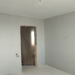 Pokój po świeżym pomalowaniu na szaro, widoczne wystające kable ze ściany i sufitu, oraz surowy otwór drzwiowy.