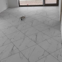 BUD VAS VAASYL FLORESKUL - Wyłożona jasnymi płytkami podłoga z marmurkowym wzorem w nowym mieszkaniu, widoczne kable elektryczne na podłodze, przygotowane do dalszych prac wykończeniowych.