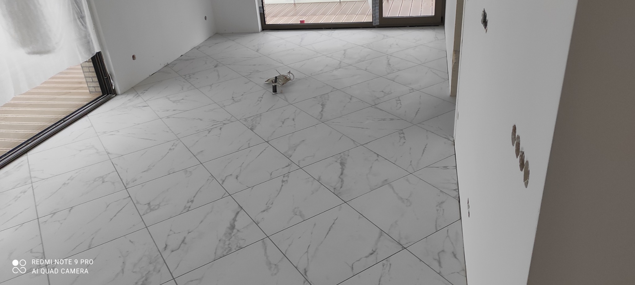 Wyłożona jasnymi płytkami podłoga z marmurkowym wzorem w nowym mieszkaniu, widoczne kable elektryczne na podłodze, przygotowane do dalszych prac wykończeniowych.