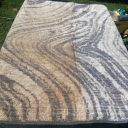 PHU MICHAŁ Michał Maciszewski - Dywan z abstrakcyjnym wzorem, widoczna różnica w czystości między wypraną a brudną częścią, obok żółty odkurzacz piorący na trawie.