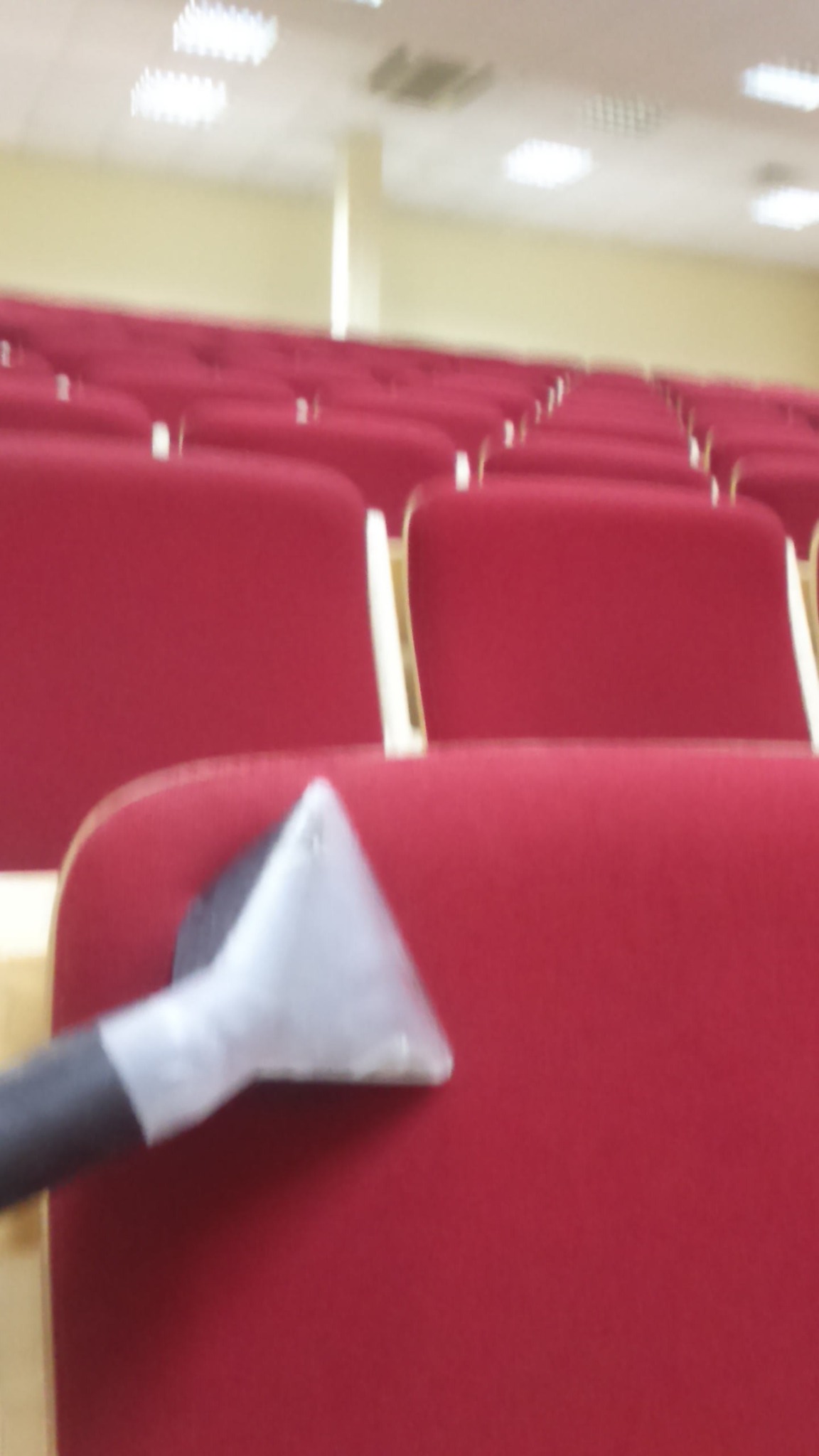 Czyszczenie czerwonych, tapicerowanych krzeseł w sali konferencyjnej za pomocą odkurzacza piorącego z przezroczystą końcówką.