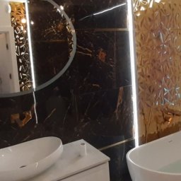 Bud Vas Vasyl Floreskul - Elegancka łazienka z owalnym lustrem, marmurowymi płytkami w odcieniach bieli i czerni, złotymi akcentami oraz wolnostojącą wanną wypełnioną wodą.