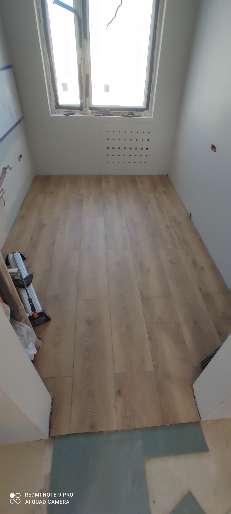 Ułożone panele podłogowe w pomieszczeniu z oknem dachowym w Koszalinie, widoczny fragment narzędzia do cięcia paneli.