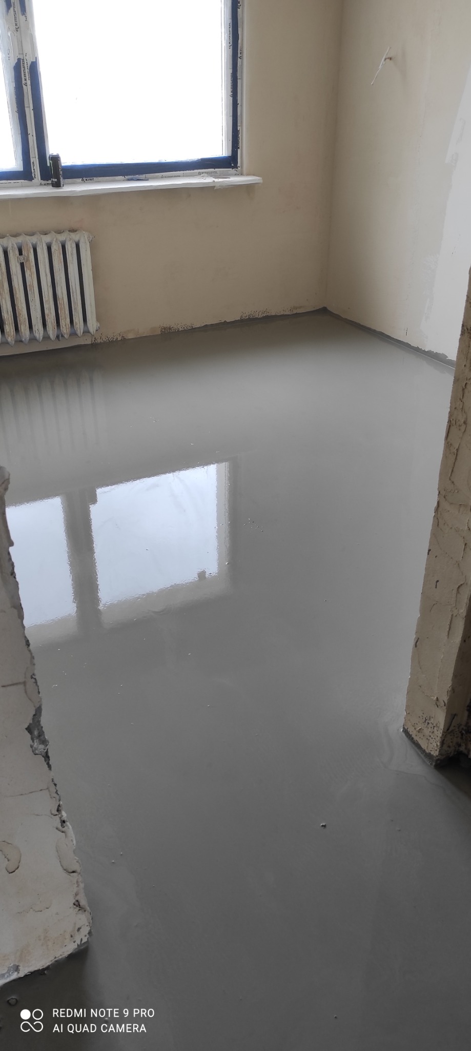 Świeżo wylana, gładka wylewka samopoziomująca na podłodze w pokoju, z widocznym odbiciem okna.