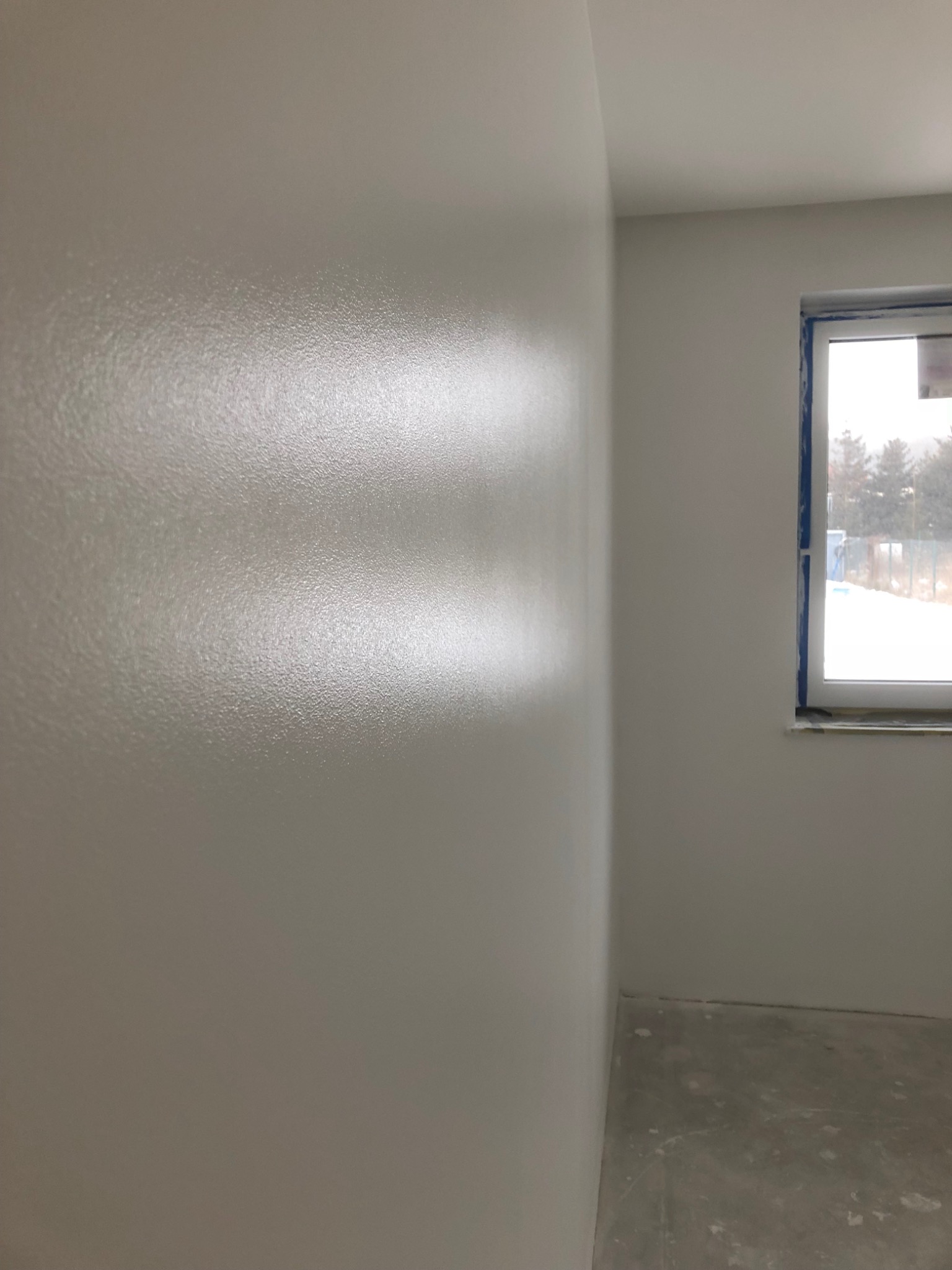 Świeżo pomalowane na biało ściany w pokoju z oknem, widoczne niedoskonałości powierzchni przed ostatecznym wykończeniem.