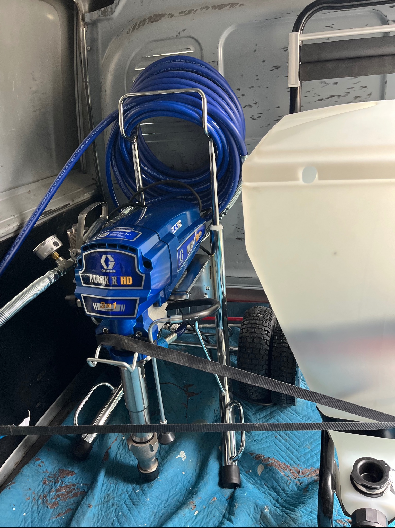 Agregat malarski Graco Mark X HD z niebieskim wężem wysokociśnieniowym, przewożony w busie na niebieskiej macie ochronnej.