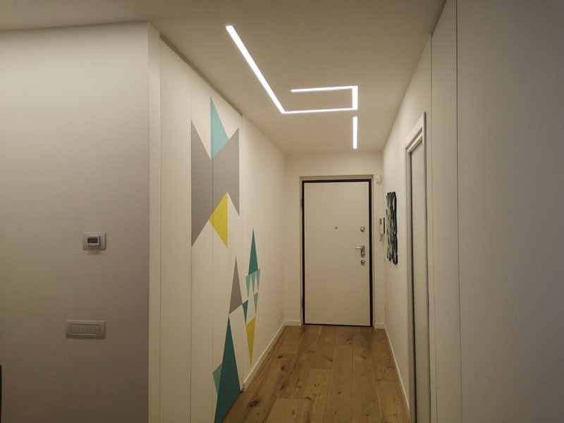 Nowoczesny przedpokój z zabudową szafy z geometrycznym wzorem, drewnianą podłogą i liniowym oświetleniem LED na suficie.