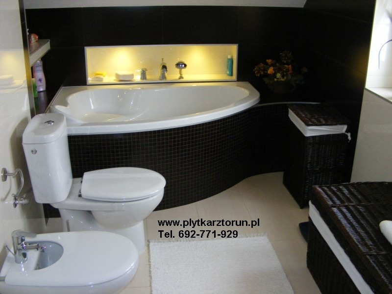 Nowoczesna łazienka z czarno-białymi płytkami mozaikowymi, owalną wanną z podświetlaną wnęką na kosmetyki, białą armaturą (toaleta i bidet) oraz plecionymi koszami na pranie. Na podłodze biały...