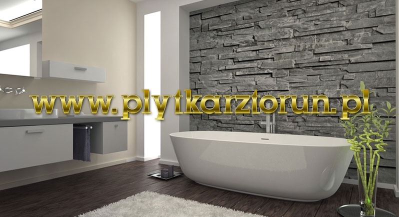 Nowoczesna łazienka z wolnostojącą wanną na tle ściany wyłożonej szarym kamieniem dekoracyjnym, drewniana podłoga i biała szafka pod umywalką, dekoracja roślinna w wazonie.