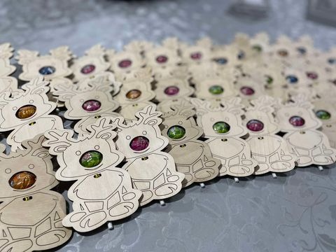 Ręcznie robione drewniane renifery z cukierkami zamiast nosa, leżące na szarym tle.