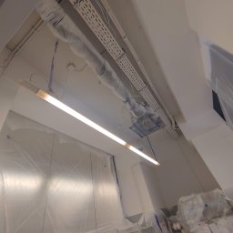 Kompleksowe Wykończenie Wnętrz Grzegorz Dewicki - Przygotowania do prac malarskich w biurze: zabezpieczone folią ściany, sufit z instalacjami owiniętymi folią ochronną i oświetlenie liniowe.