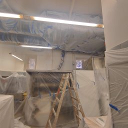 Kompleksowe Wykończenie Wnętrz Grzegorz Dewicki - Przygotowania do prac wykończeniowych w pomieszczeniu biurowym, meble i elementy wyposażenia zabezpieczone folią malarską, widoczna drabina malarska.