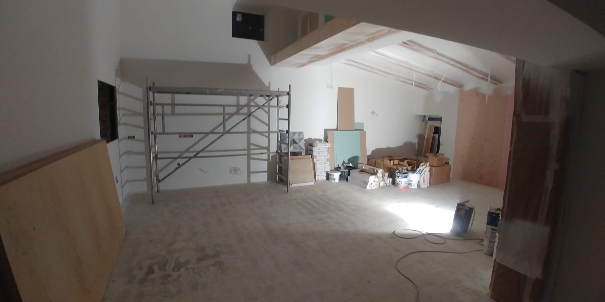 Wnętrze w trakcie remontu: widoczne rusztowanie, materiały budowlane, ściany przygotowane do malowania, sufit z odsłoniętą konstrukcją, podłoga w trakcie przygotowania.