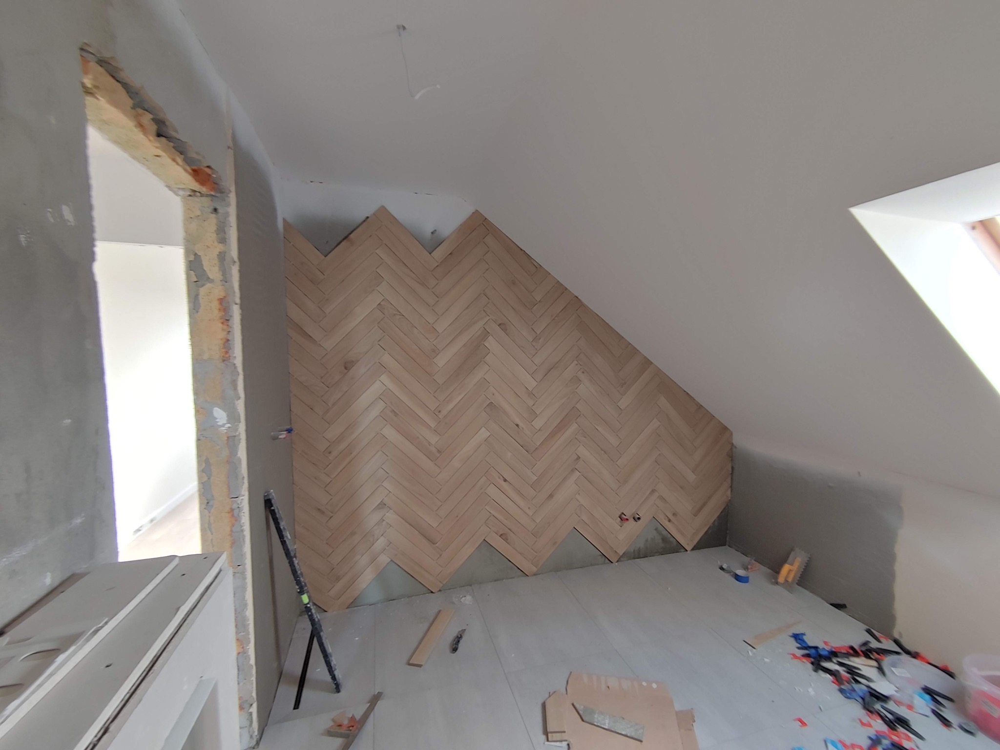 Montaż drewnianej okładziny ściennej w jodełkę na poddaszu w Poznaniu, widoczne niedokończone fragmenty i narzędzia glazurnicze na podłodze.