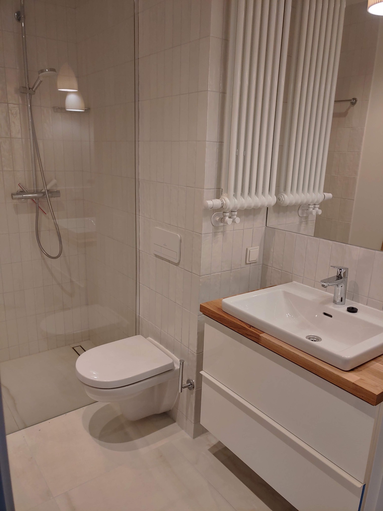 Nowoczesna łazienka z kabiną prysznicową typu walk-in, podwieszaną toaletą i umywalką nablatową z drewnianym blatem.