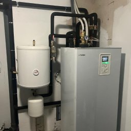 BPOWER SP.Z O.O - Instalacja pompy ciepła NIBE z zasobnikiem ciepłej wody i rurami w piwnicy z surowymi ścianami.