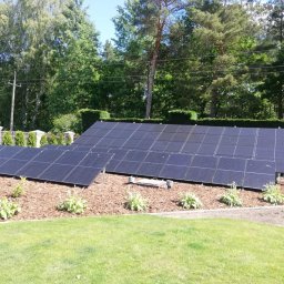 BPOWER SP.Z O.O - Instalacja paneli słonecznych na posesji z trawnikiem i ozdobnymi roślinami na korze, widoczne słupy elektryczne w tle.