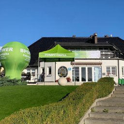 BPOWER SP.Z O.O - Stoisko promocyjne z napisem 'Pompy Ciepła' pod zielonym namiotem, obok dmuchana reklama 'Fotowoltaika' na tle budynku klubu golfowego w słoneczny dzień.