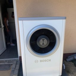 BPOWER SP.Z O.O - Biała pompa ciepła marki Bosch zamontowana przy wejściu do domu, z widocznymi elementami instalacji.