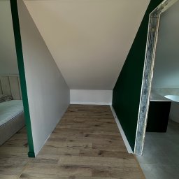 ROMAN MATUSHCHAK ARMBUILDING - Wykończone poddasze ze skośnymi ścianami pomalowanymi na biało i butelkową zieleń. Widoczna podłoga z paneli i fragment łazienki z wanną. Metalowa futryna.
