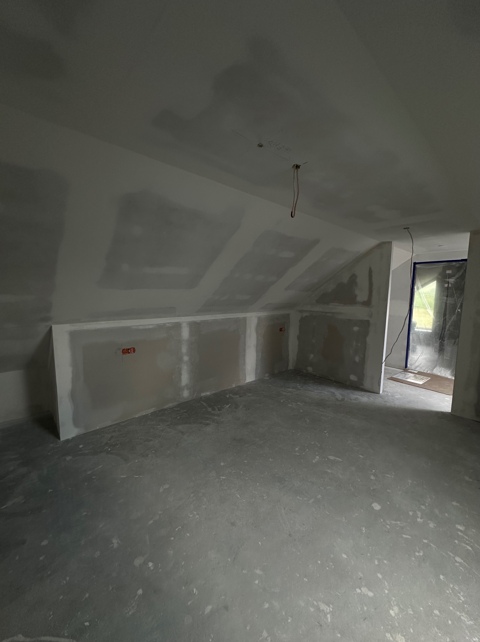 Poddasze z oknem, ściany wykończone płytami gipsowo-kartonowymi przed szpachlowaniem, widoczne puszki elektryczne, surowa wylewka podłogowa, przygotowanie do prac wykończeniowych.