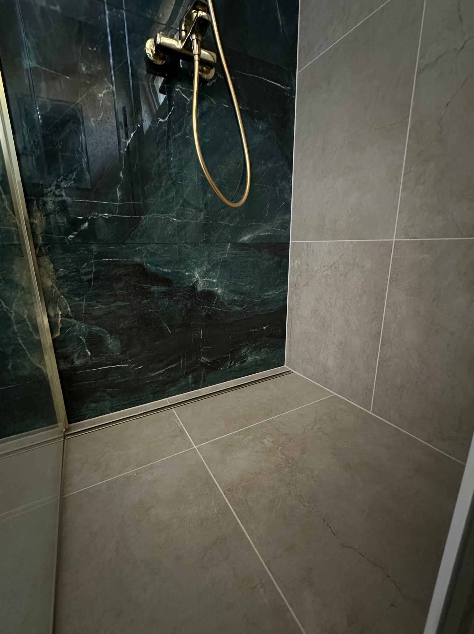 Nowoczesna kabina prysznicowa z zielonym marmurem i złotą armaturą. Szare płytki podłogowe i ścienne tworzą minimalistyczne wykończenie łazienki.