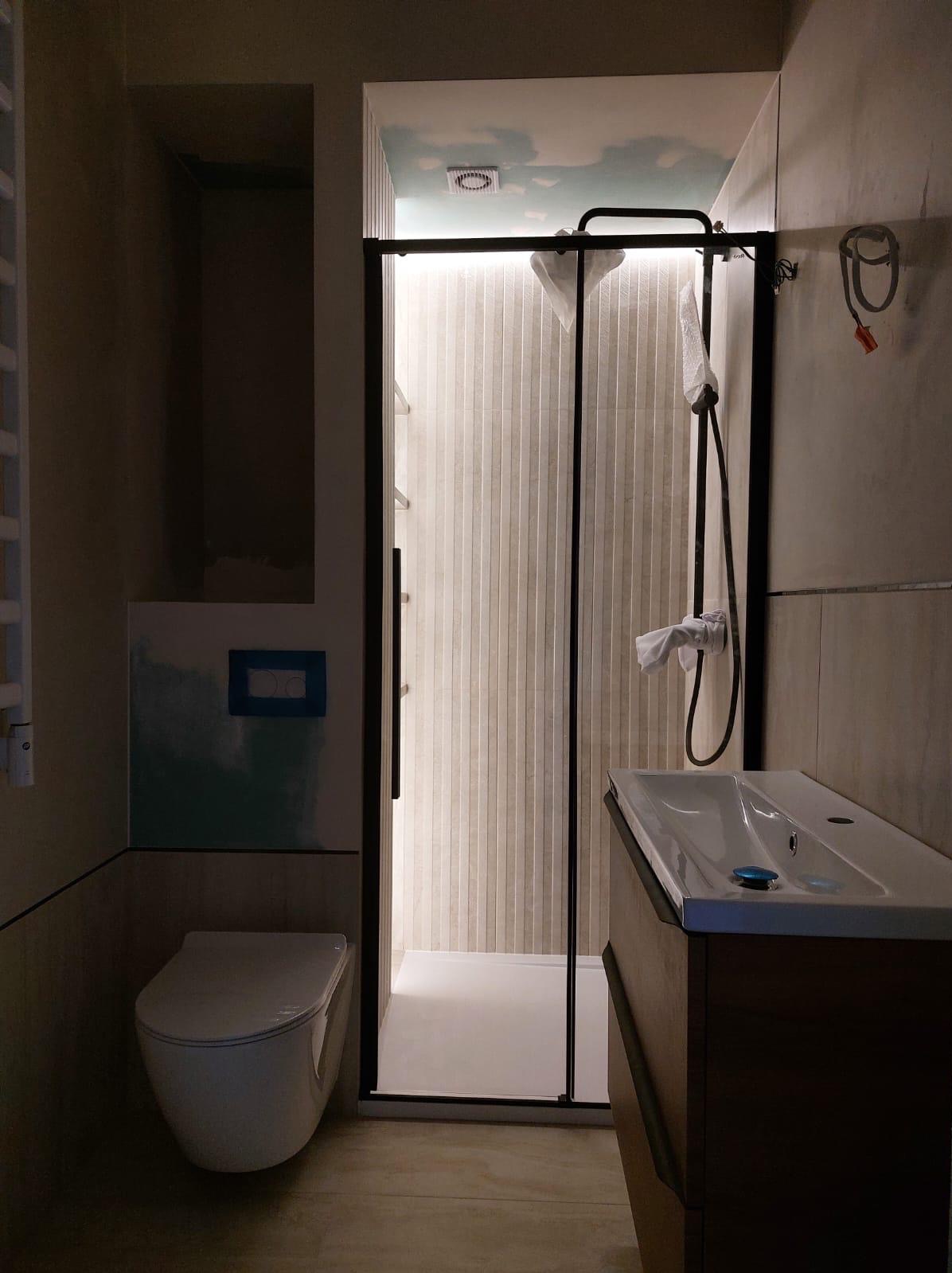 Nowoczesna łazienka z kabiną prysznicową typu walk-in, umywalką w drewnianej szafce i podwieszaną toaletą. Na suficie widoczny motyw nieba z chmurami.