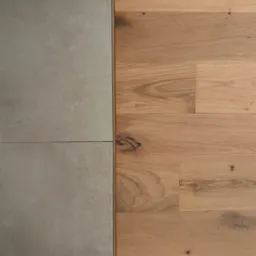 Połączenie szarych, matowych płytek podłogowych i drewnianej podłogi z widocznymi sękami, oddzielone cienką, metalową listwą.