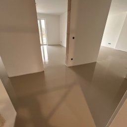 WOODEAL SPÓŁKA Z OGRANICZONĄ ODPOWIEDZIALNOŚCIĄ - Świeżo wylana, beżowa posadzka w jasnym, pustym pomieszczeniu z widocznymi instalacjami elektrycznymi w ścianach. Gładka powierzchnia odbija światło.