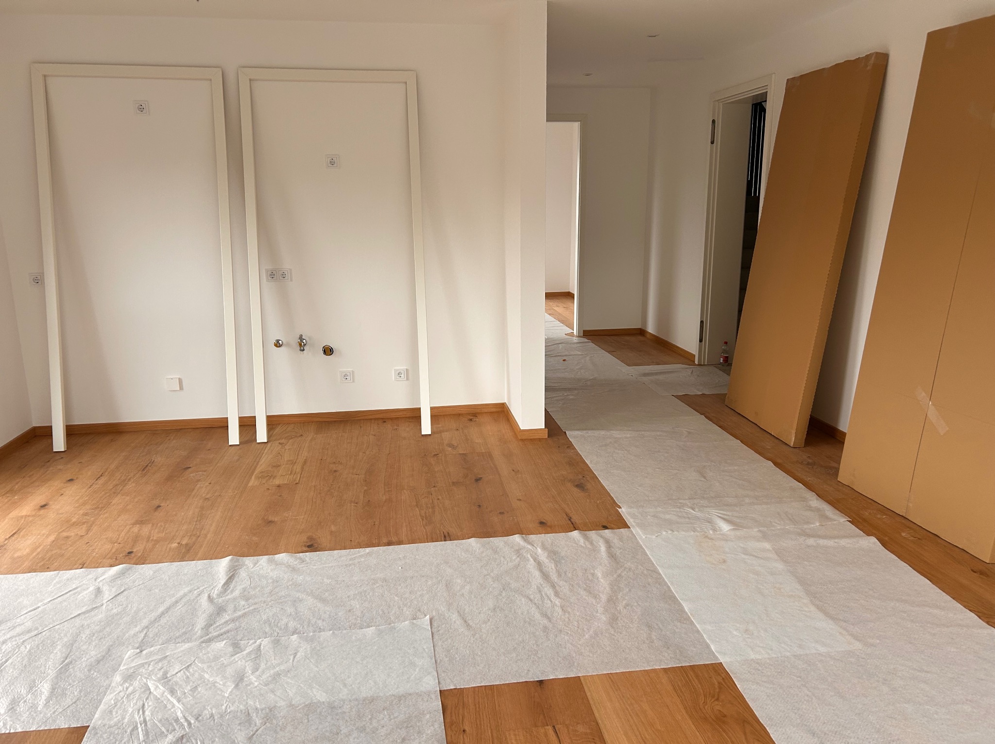 Przygotowanie do montażu drzwi: ościeżnice ustawione w surowym wnętrzu, podłoga zabezpieczona folią ochronną, widoczne instalacje elektryczne i hydrauliczne.