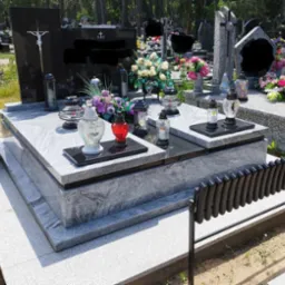 Podwójny nagrobek z jasnoszarego granitu z czarnymi tablicami, ozdobiony kwiatami w wazonach i lampionami na cmentarzu.