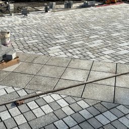 SULOWSKI GROUP SPÓŁKA Z OGRANICZONĄ ODPOWIEDZIALNOŚCIĄ - Układanie kostki granitowej: widok na fragment powierzchni z ułożoną kostką granitową w trzech różnych wzorach, obok stos kostki przygotowanej do ułożenia i narzędzia.