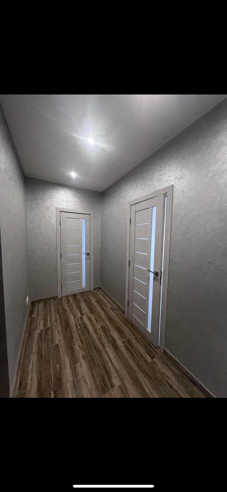 Korytarz po remoncie z drewnopodobną podłogą, szarymi ścianami z efektem dekoracyjnym i dwoma białymi drzwiami z przeszkleniami.