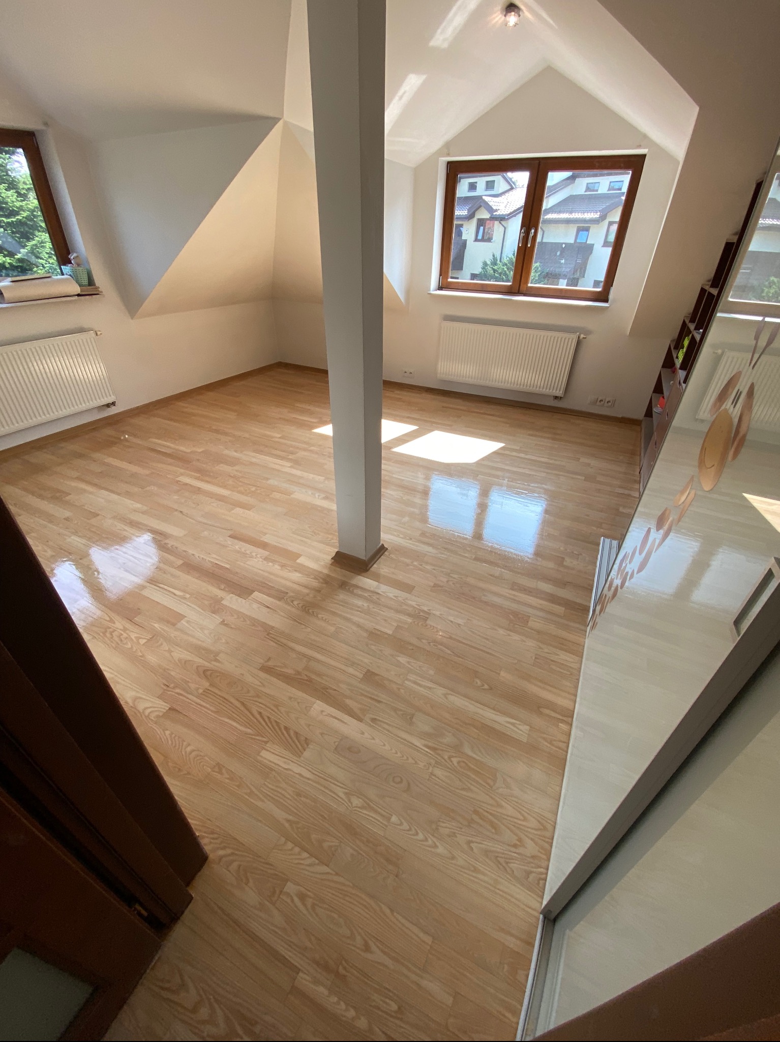 Jasny parkiet w pokoju na poddaszu z kolumną nośną, widoczne refleksy światła słonecznego na podłodze.