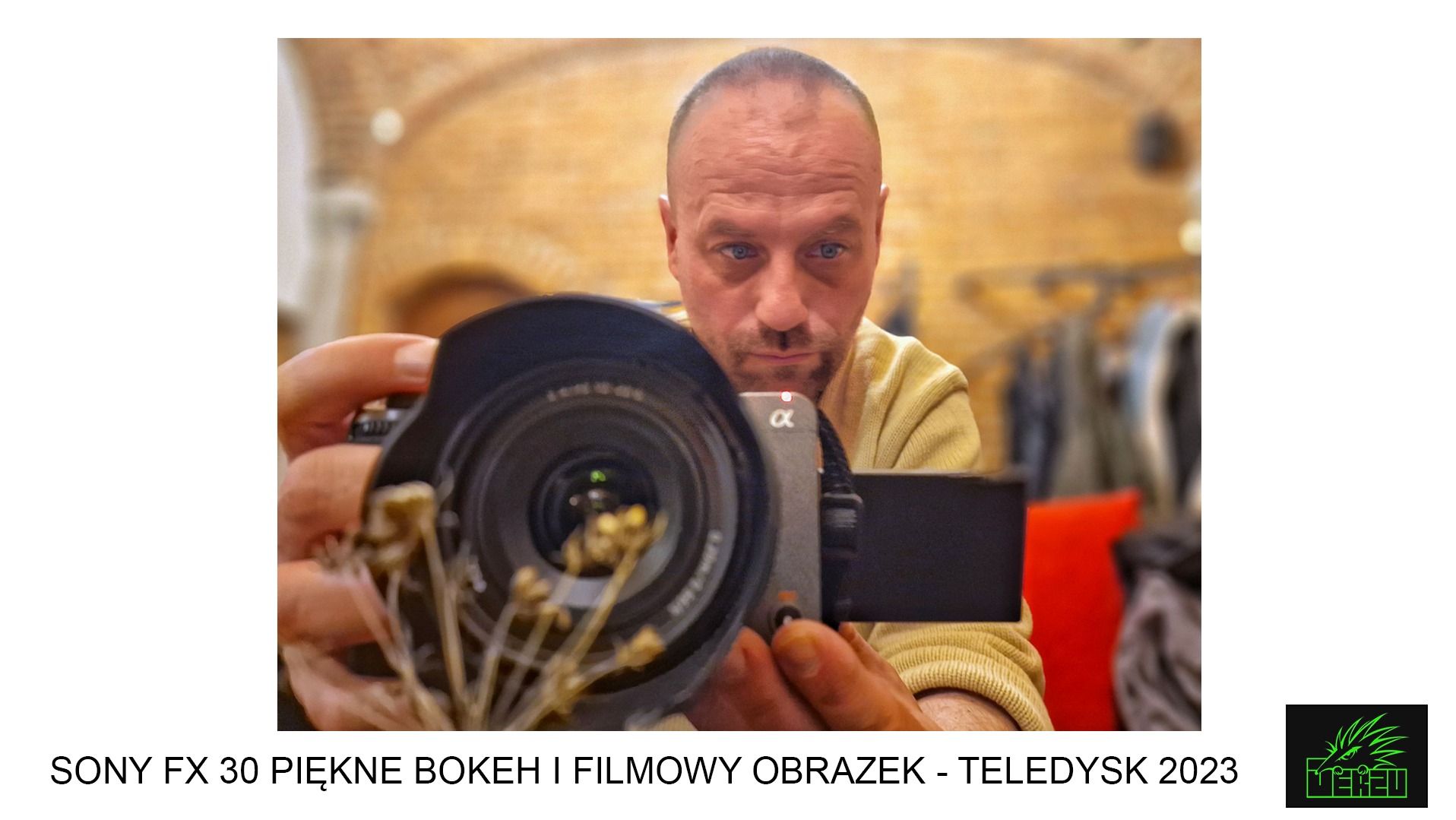 Mężczyzna z niebieskimi oczami filmuje kamerą Sony FX30 z widocznym obiektywem i ekranem, w tle rozmyte wnętrze z ubraniami.