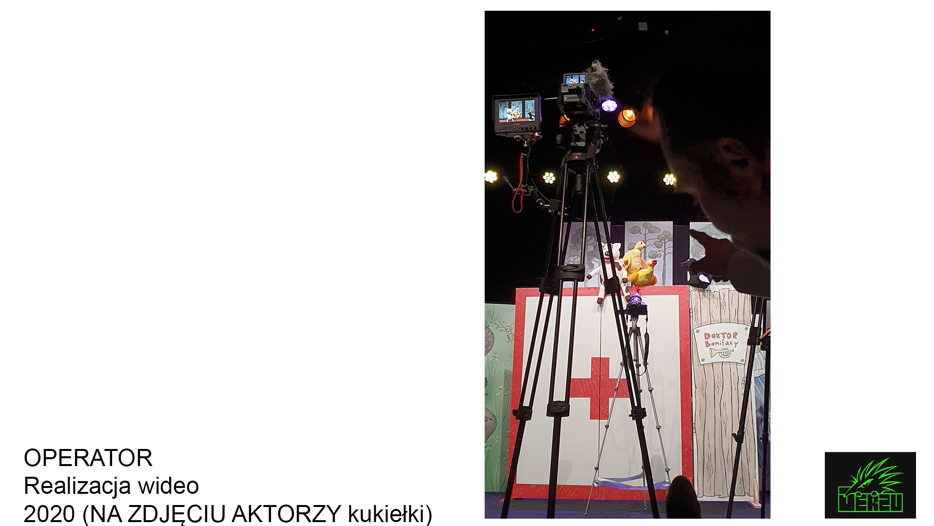 Kamera na statywie filmująca scenę lalkową z aktorem wskazującym na kukiełki, oświetlenie sceniczne w tle.