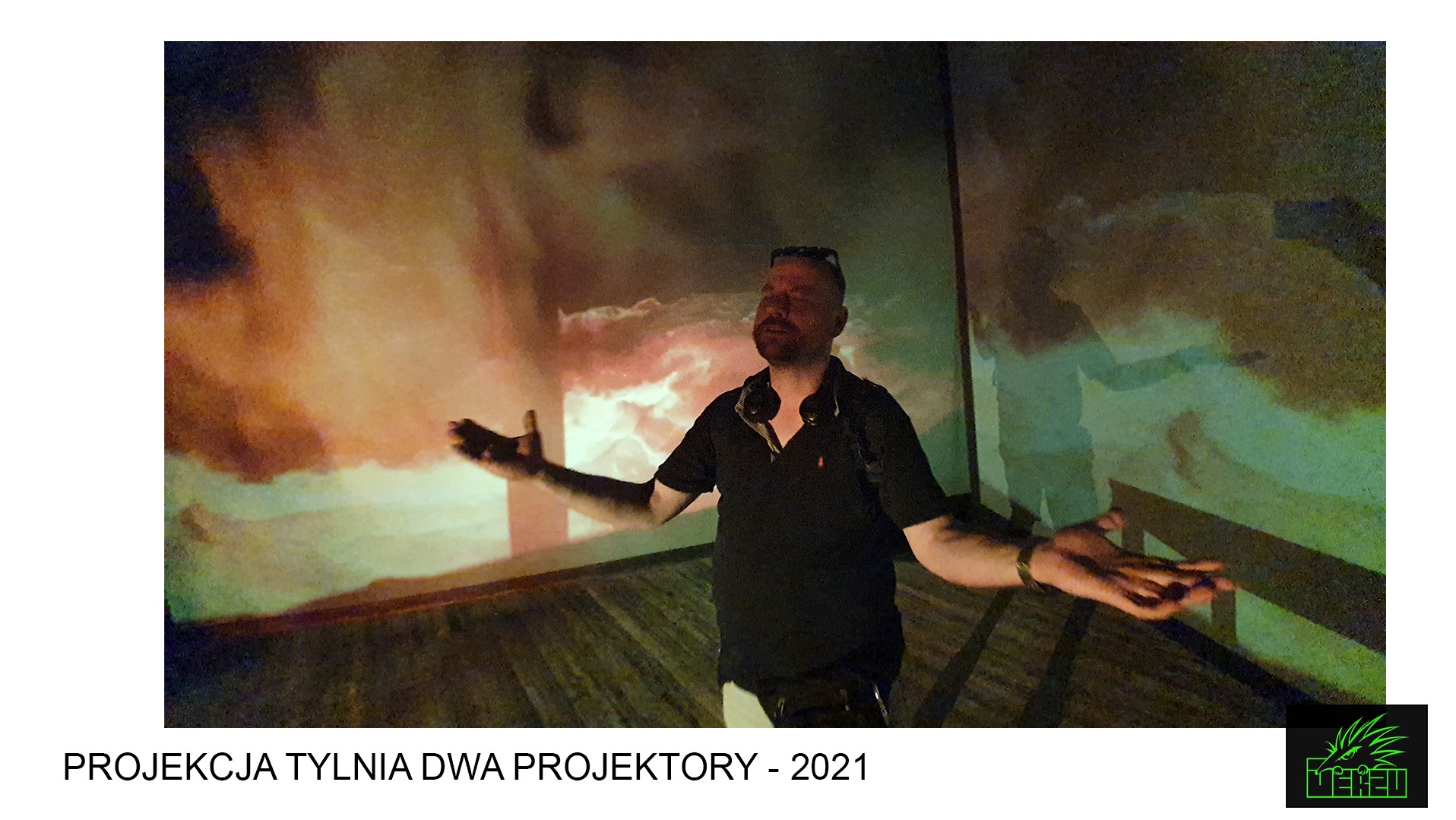 Mężczyzna z rozłożonymi rękami stoi na tle projekcji przypominającej burzę z piorunami.