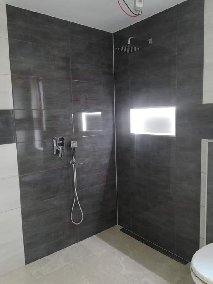 Nowoczesna kabina prysznicowa z ciemnymi, strukturalnymi płytkami, wnęką z podświetleniem i odpływem liniowym w podłodze.