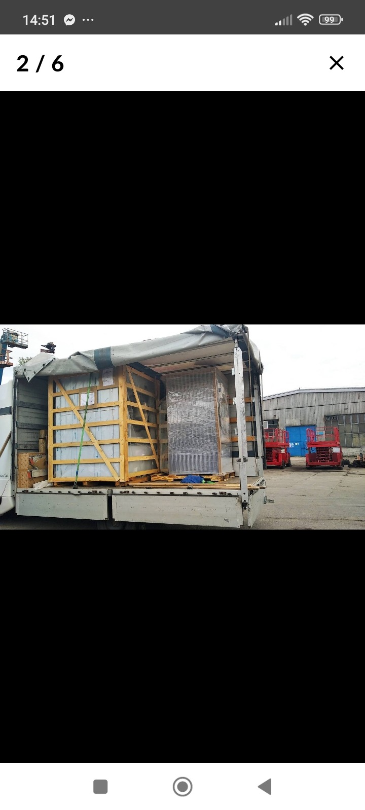 Dwa ładunki, jeden w drewnianej skrzyni zabezpieczonej pasami, drugi owinięty folią, załadowane na otwartą platformę samochodu ciężarowego z plandeką w trakcie transportu.