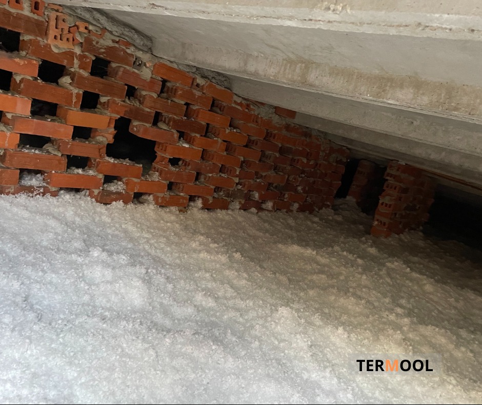 Poddasze ocieplone białą wełną mineralną Termoool, widoczna ceglana ściana z otworami wentylacyjnymi i betonowy strop.