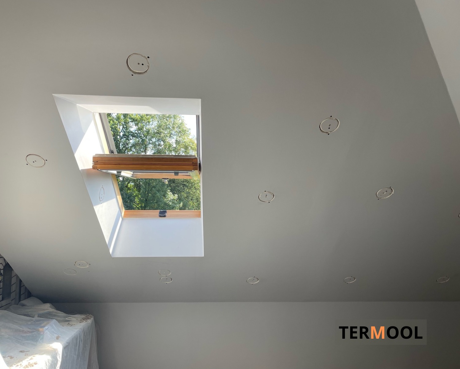 Poddasze z oknem dachowym i przygotowanymi otworami na oświetlenie, widoczna folia ochronna na elementach wyposażenia.