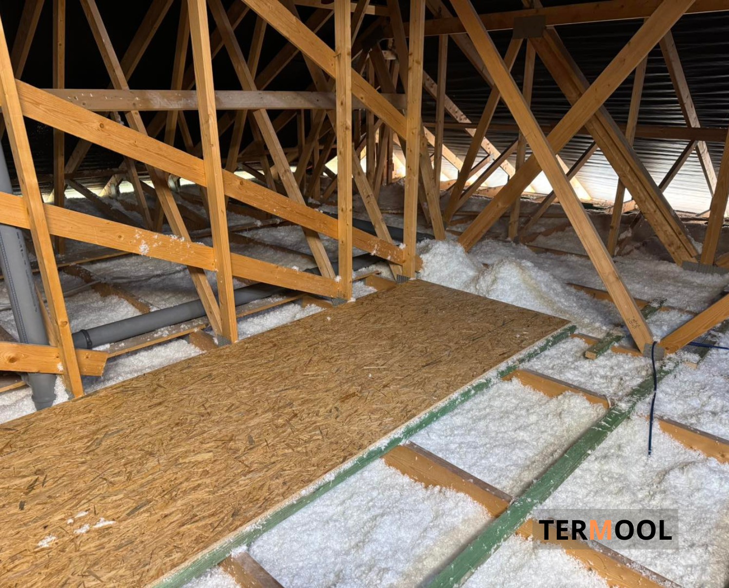 Poddasze z drewnianą konstrukcją i izolacją z białej wełny mineralnej. Fragment płyty OSB na podłodze. Widoczne rury wentylacyjne.