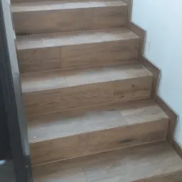 Schody wyłożone płytkami imitującymi drewno, z widocznymi listwami wykończeniowymi przy ścianie.