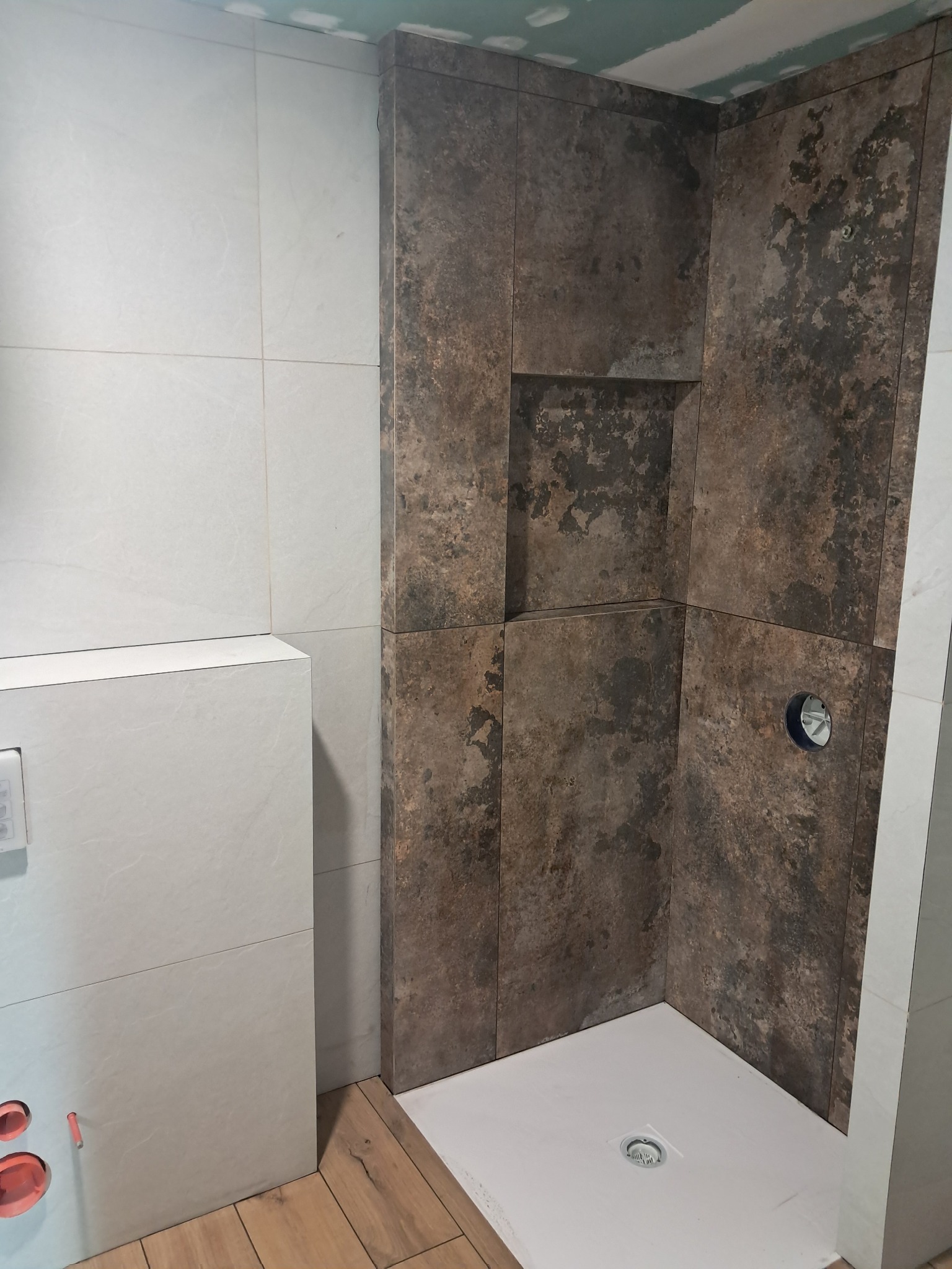 Wnętrze kabiny prysznicowej z brązowymi płytkami imitującymi kamień i wnęką, obok zabudowa toalety z jasnych płytek.