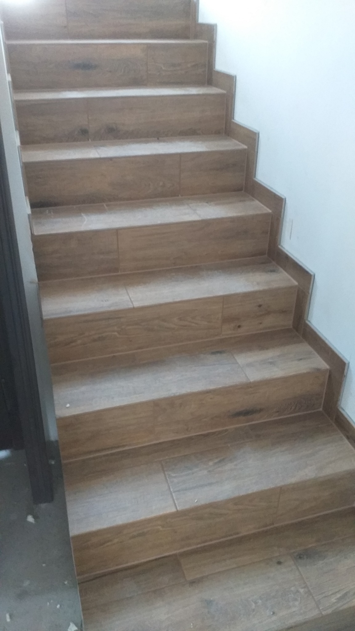 Schody wyłożone płytkami imitującymi drewno, z widocznymi listwami wykończeniowymi przy ścianie.