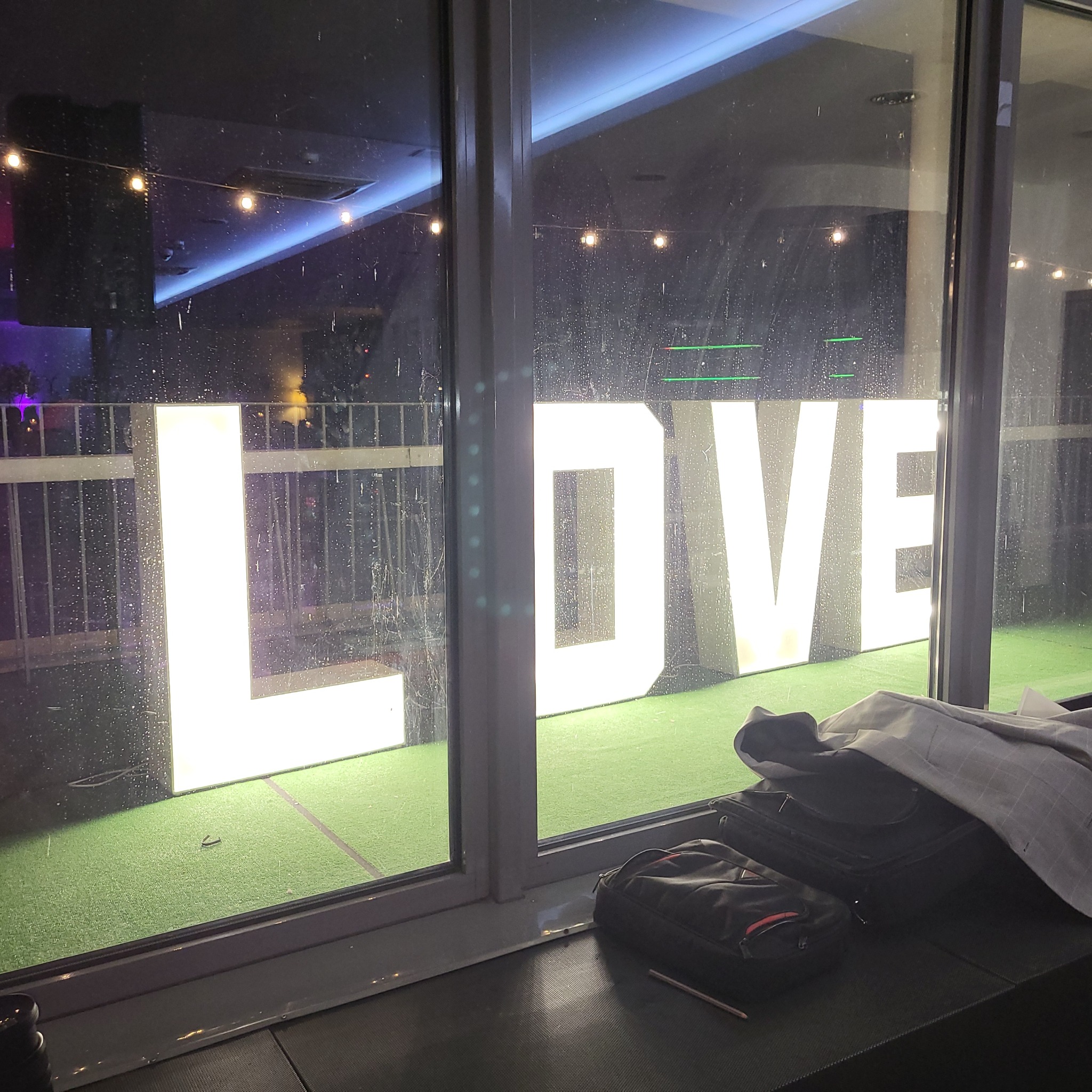 Podświetlany napis LOVE widoczny przez brudne okno, na parapecie leżą torby i marynarka.