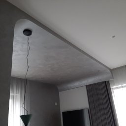 Usługi budowlane - Nowoczesne wykończenie sufitu z gładzią w odcieniach szarości w mieszkaniu w Warszawie, z widoczną lampą wiszącą i zasłonami.