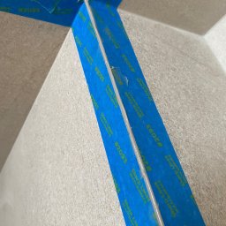Usługi budowlane - Aplikacja taśmy malarskiej Sharp Lines #2093, zabezpieczającej narożnik ściany przed malowaniem, widoczne niedoskonałości w przyklejeniu taśmy.