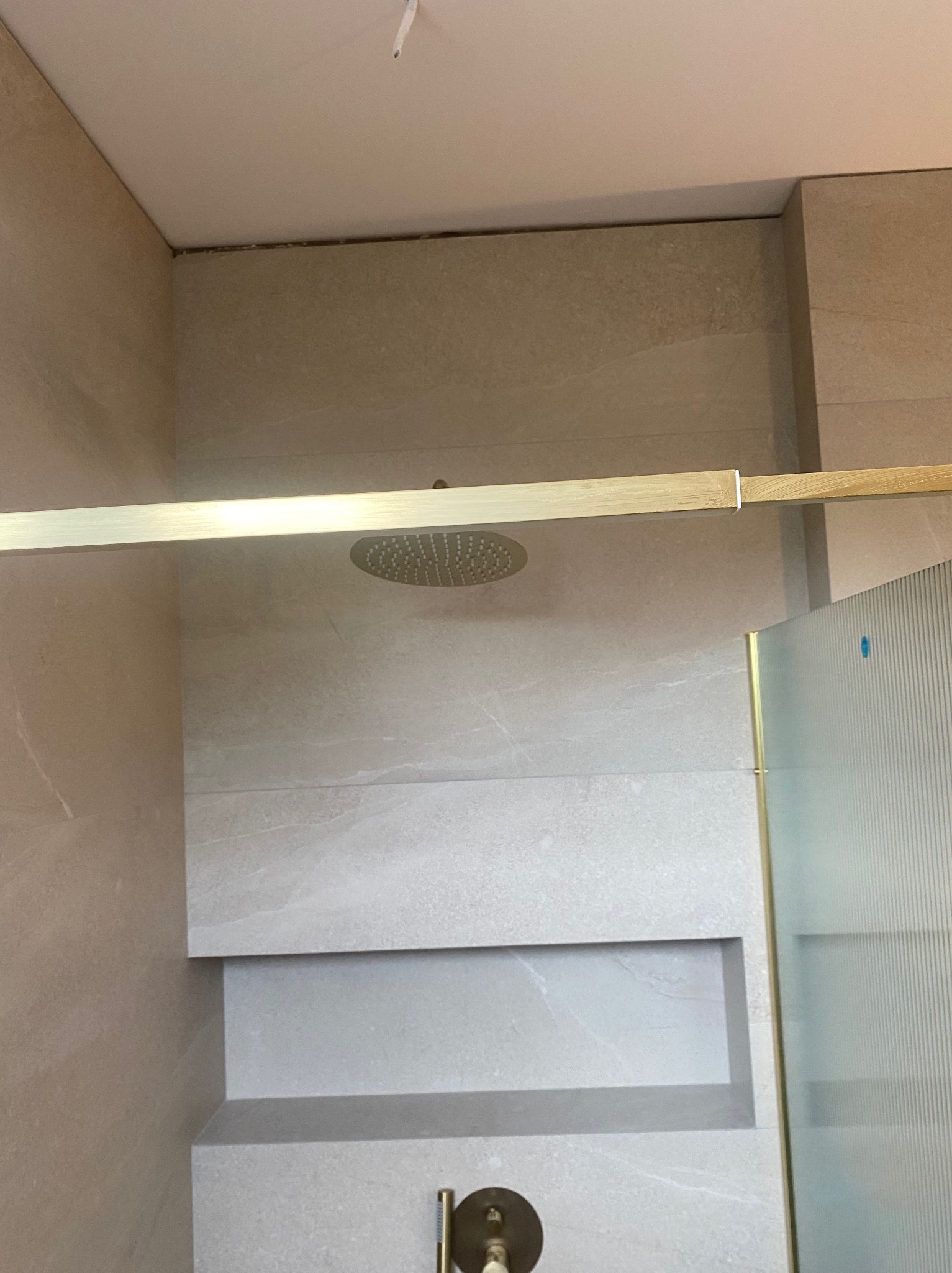 Nowoczesna kabina prysznicowa z deszczownicą i wnęką w ścianie wyłożona płytkami imitującymi kamień, złote detale wykończenia.