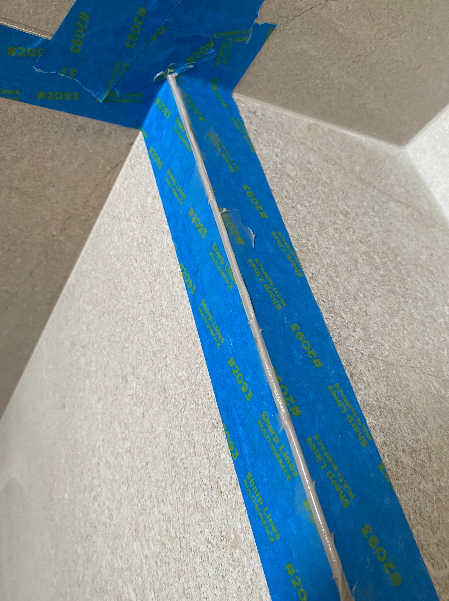 Aplikacja taśmy malarskiej Sharp Lines #2093, zabezpieczającej narożnik ściany przed malowaniem, widoczne niedoskonałości w przyklejeniu taśmy.